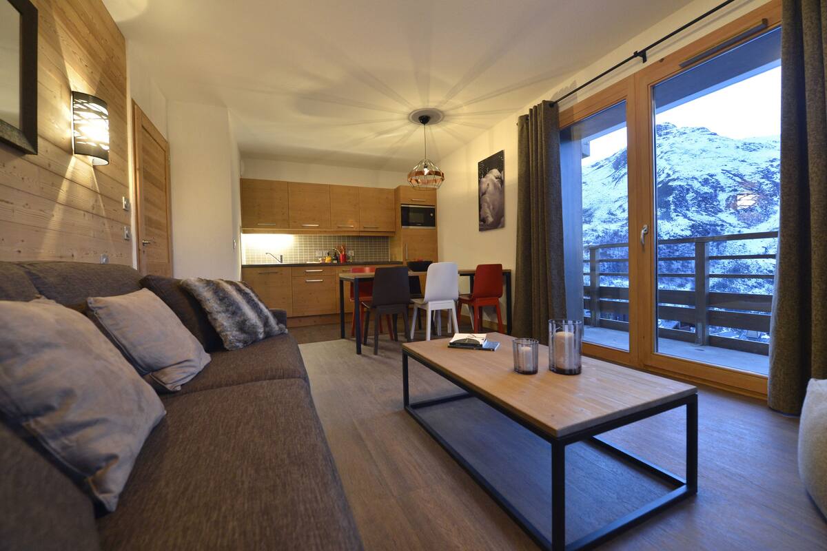A modern living room with a sofa, a dining table, and a kitchen in the background.
