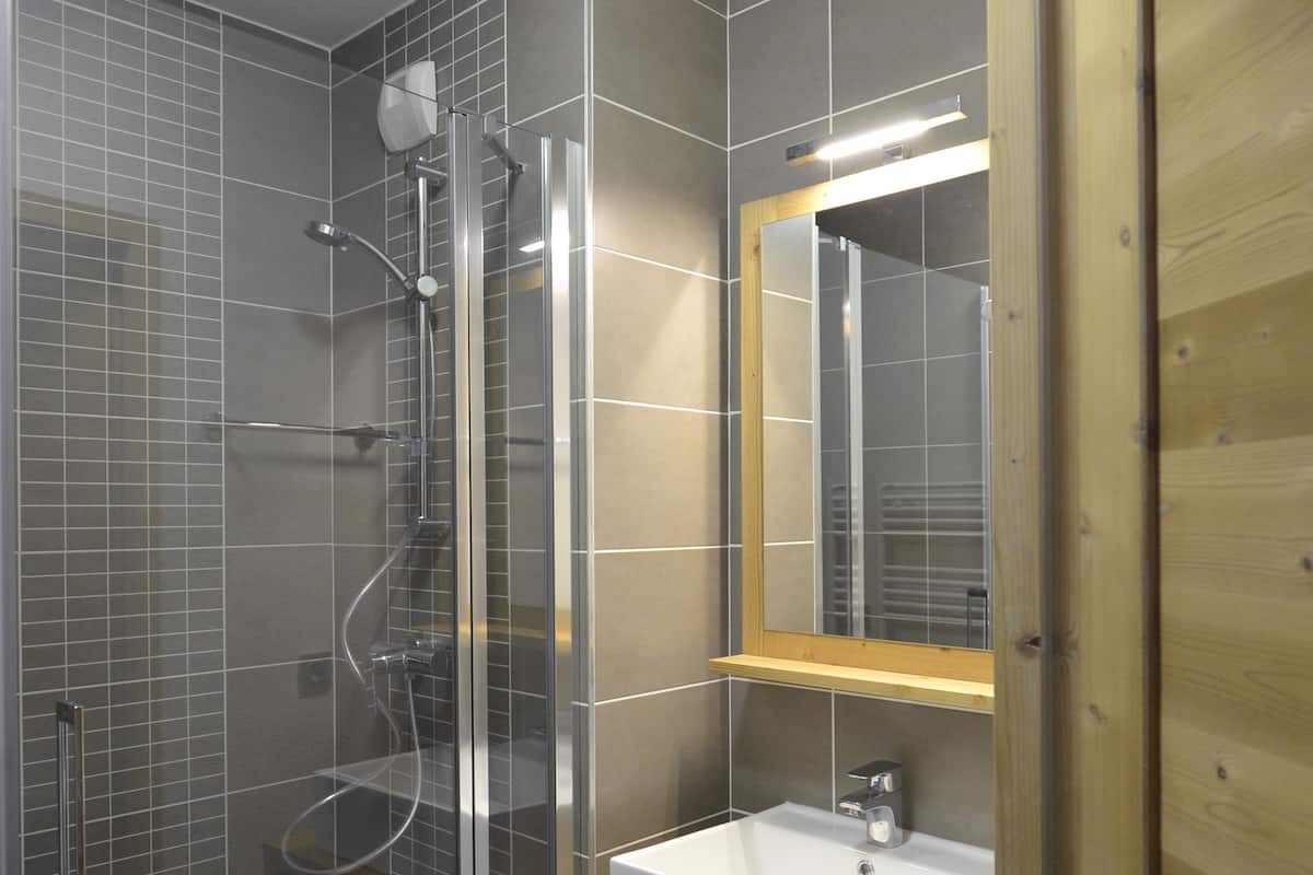 A modern bathroom with a glass shower enclosure, a white sink, and a wooden vanity.