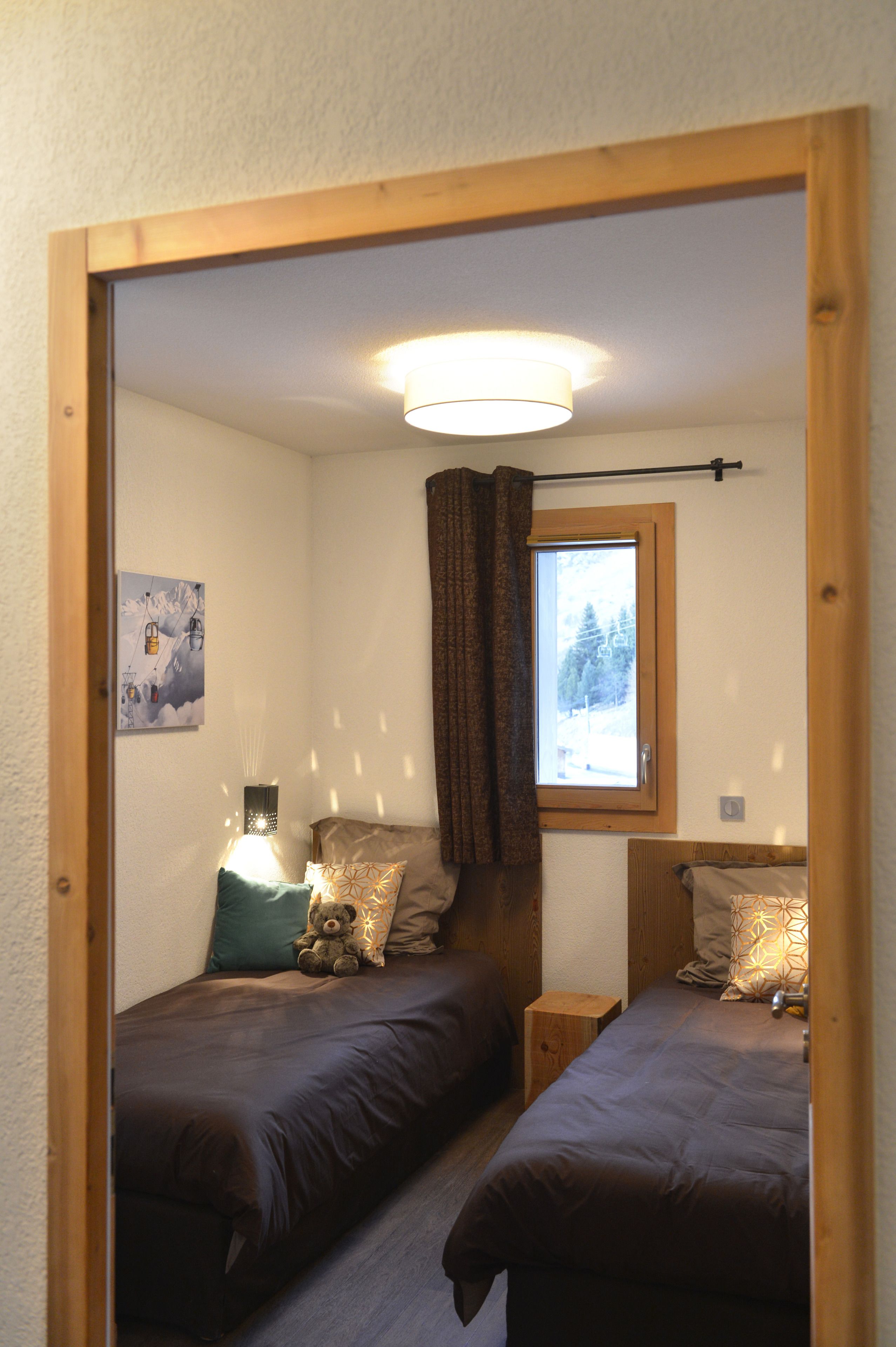 Een slaapkamer met twee bedden, een raam met uitzicht op bomen, een lamp en een teddybeer op een van de bedden.