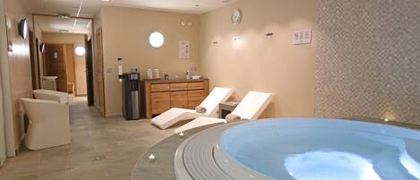 A spa room with a hot tub, lounge chairs, a wooden cabinet with toiletries, and a tiled floor.