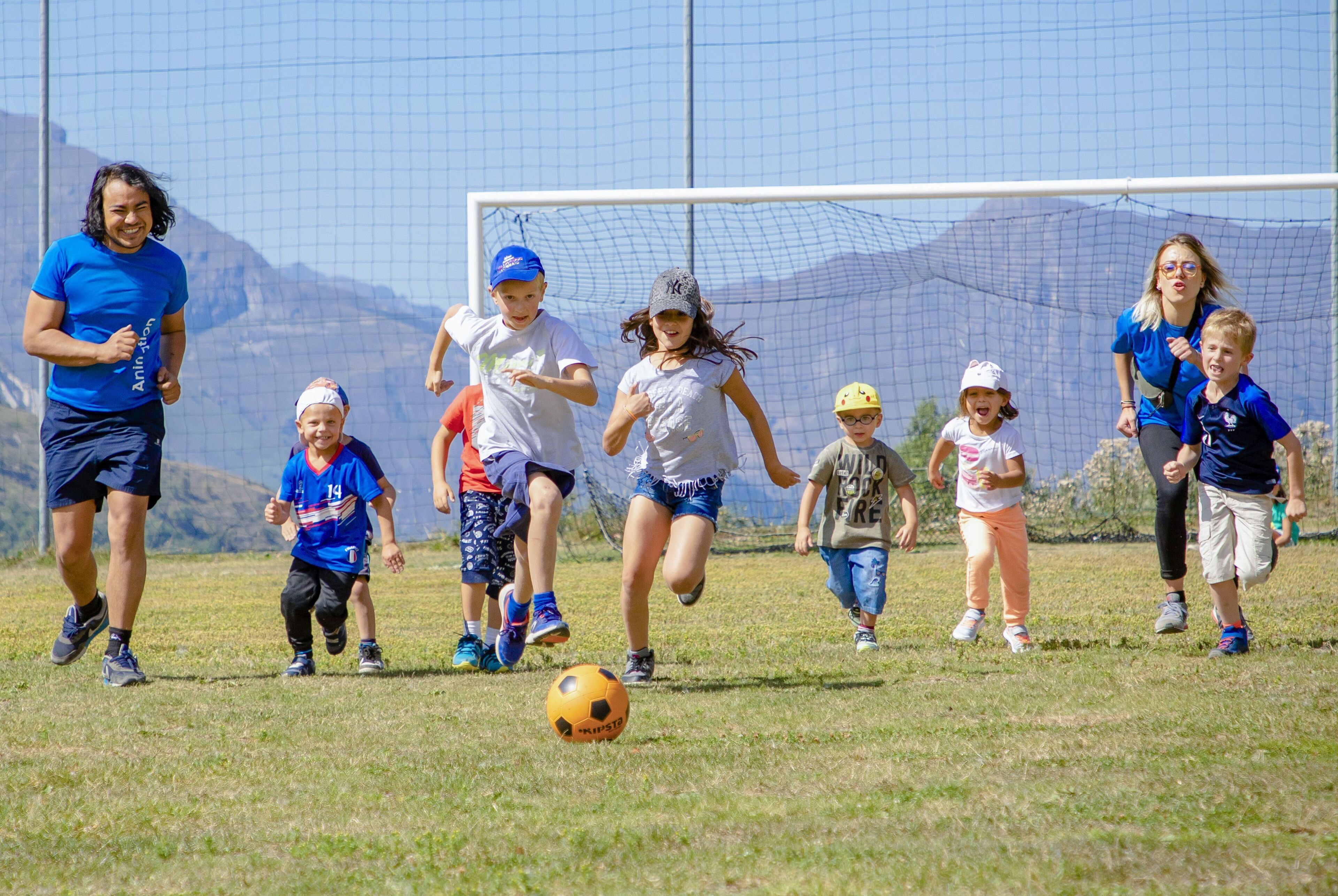 A group of children playing soccer on a grassy field with a goal post in the background.