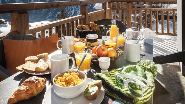 Una mesa de desayuno con comida y bebidas, con vistas a montañas nevadas.