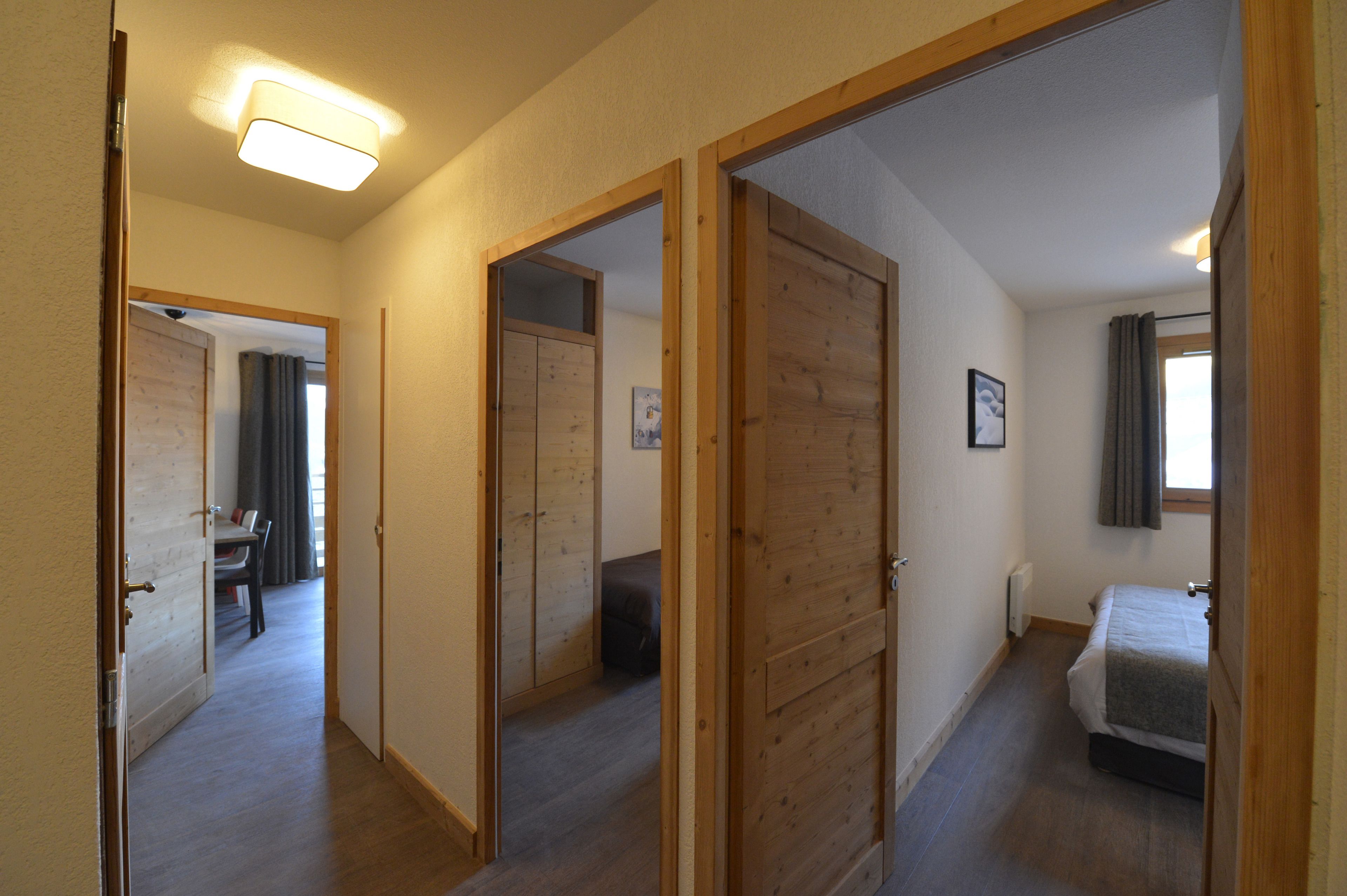 A hallway with wooden doors leading to a bedroom and a dining area.