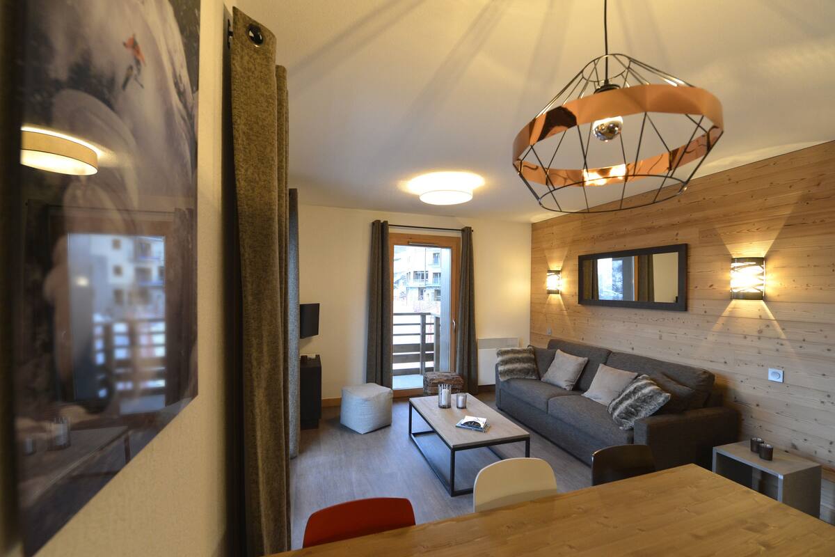 A modern living room with a wooden wall, a sofa, a coffee table, and a dining table.