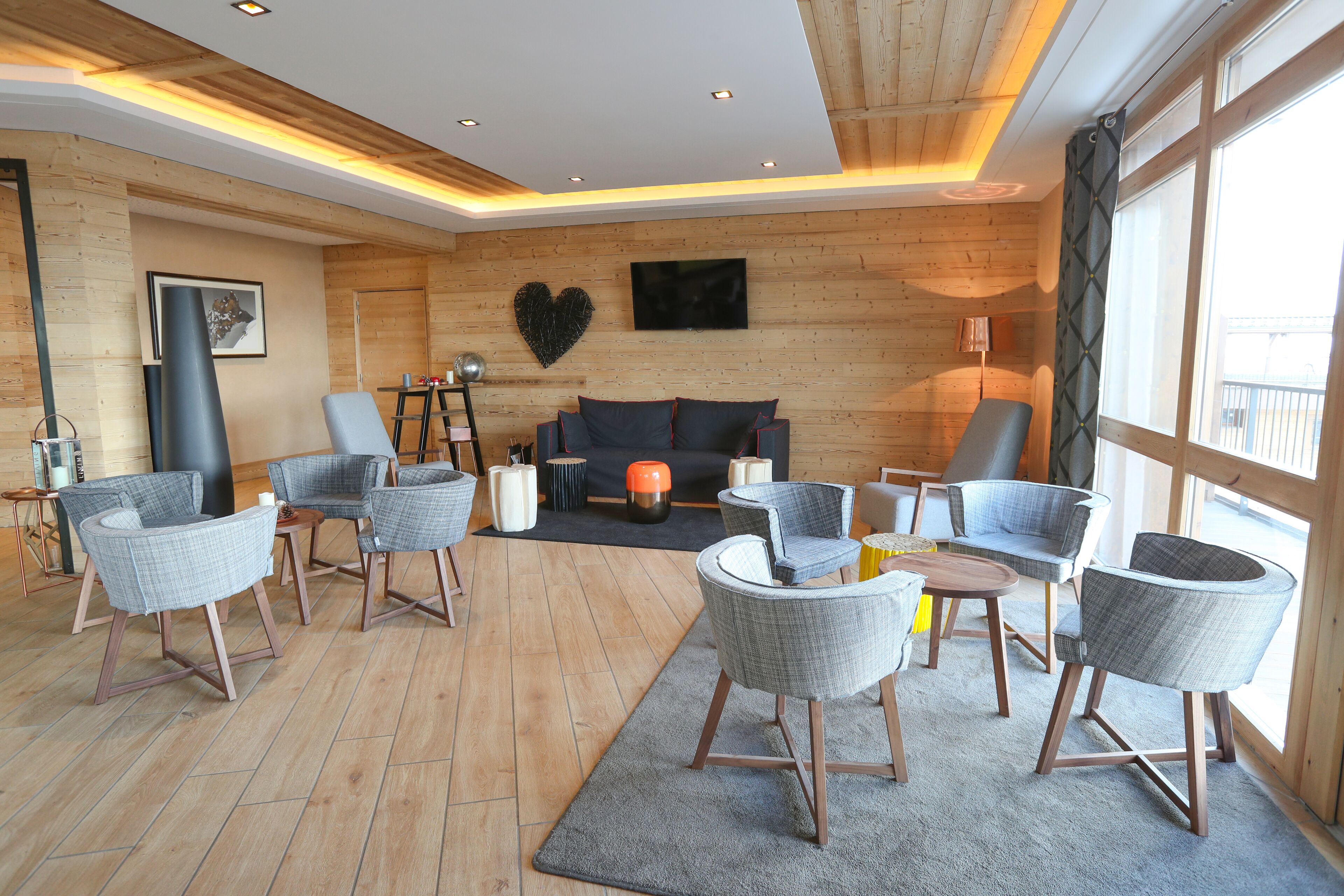 A modern living room with wooden walls, a grey sofa, and multiple grey armchairs.