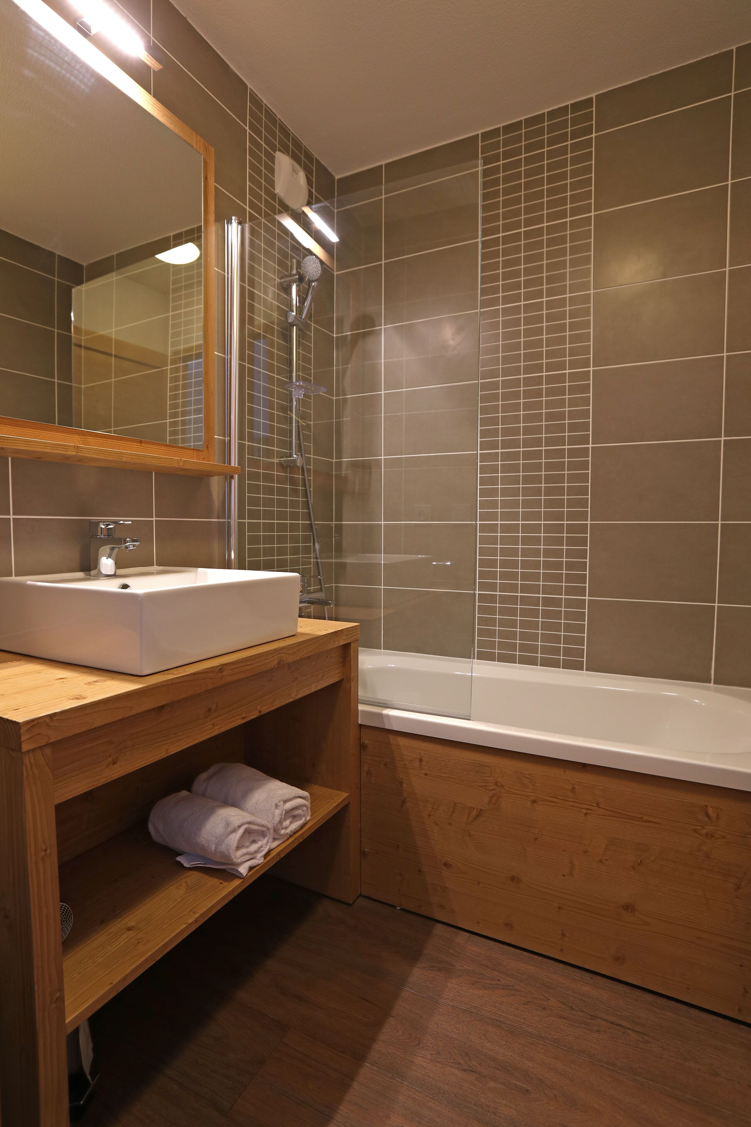 Une salle de bain avec un meuble-lavabo en bois, un lavabo blanc, un miroir, une douche et une baignoire.