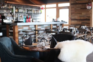 A restaurant with wooden tables and chairs, a bar in the background, and a view through large windows.