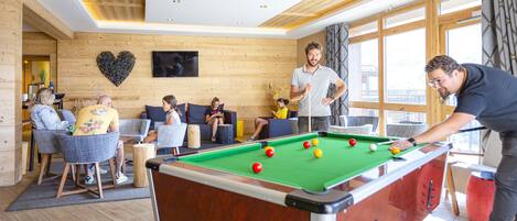 A pool table in a room with wooden walls and large windows.