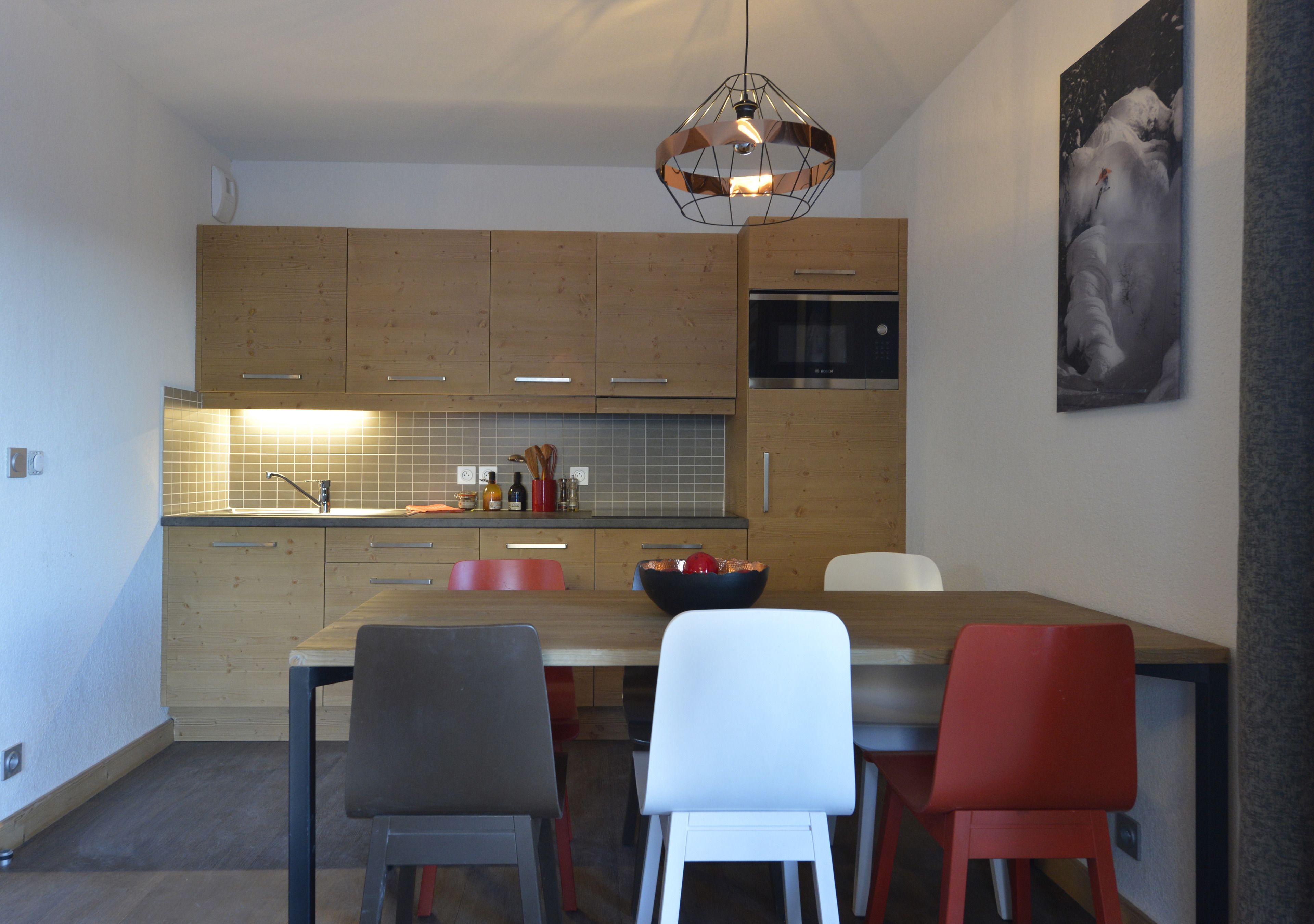 A modern kitchen with wooden cabinets, a stainless steel oven, and a dining area with a wooden table and chairs.