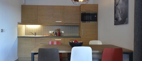 A modern kitchen with wooden cabinets, a stainless steel oven, and a dining area with a wooden table and chairs.