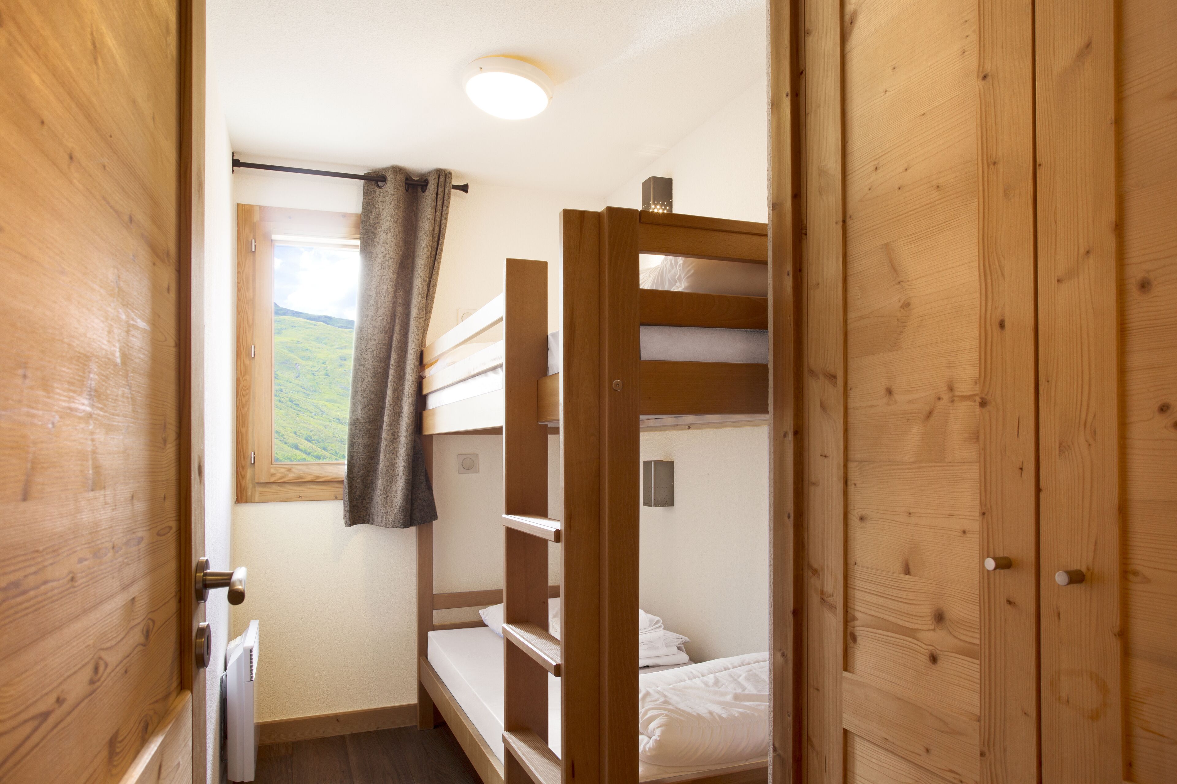 A compact room with bunk beds, a window with a curtain, and wooden walls.
