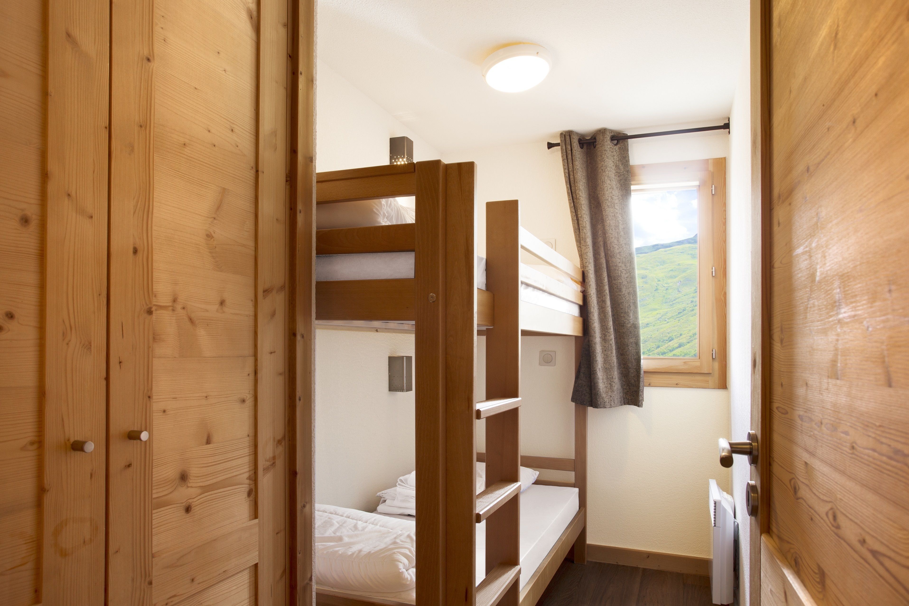 Une petite pièce avec des lits superposés, des murs en bois, une fenêtre donnant sur un paysage et une porte.