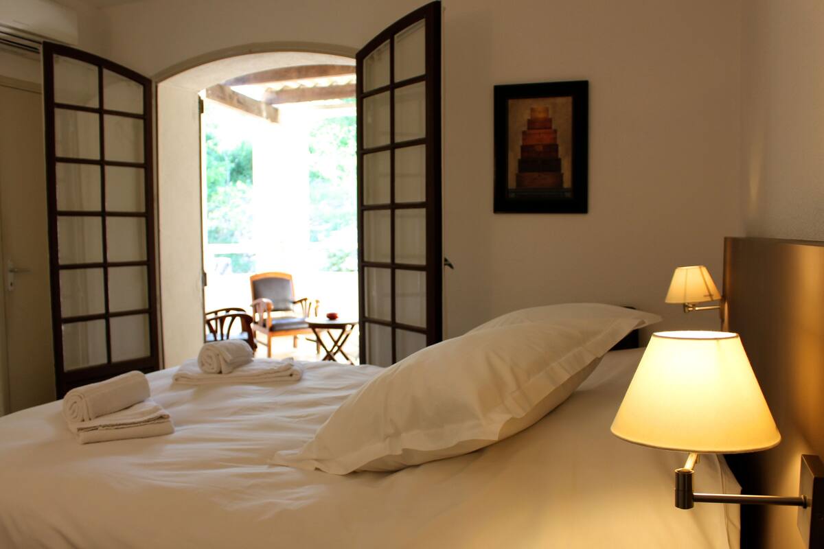 A hotel room with a bed, a lamp, a chair, and a table.