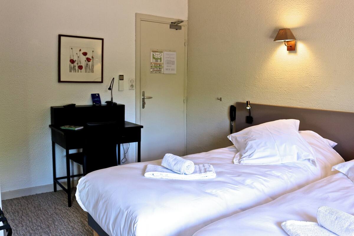 A hotel room with a bed, a desk, and a wall-mounted lamp.