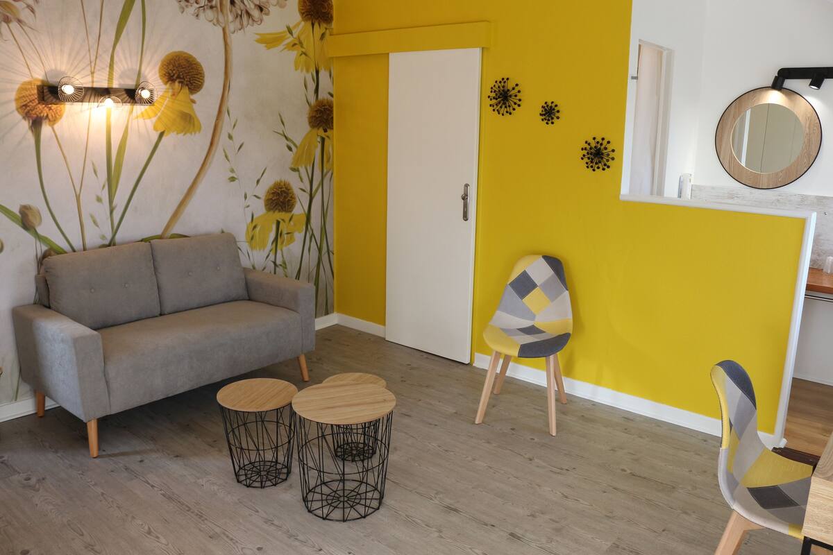 A room with a sofa, two round wooden tables, a chair, and a door.