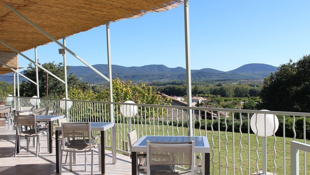 An outdoor patio with tables and chairs, a thatched roof, and a view of distant mountains. - Hôtel de Vacances de la Vignasse (Chandolas)