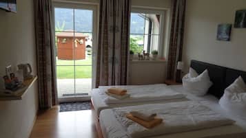 Ein Hotelzimmer mit zwei Betten, einem fensterbelaubten Fenster, einem kleinen Tisch mit Wasserkocher und Blick auf einen Garten und ein Gebäude.
