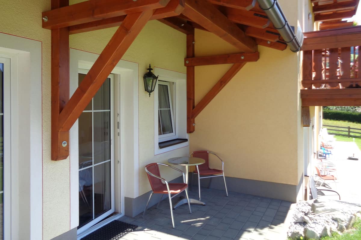 Un patio con una pérgola de madera, un vidrio y dos sillas rojas.