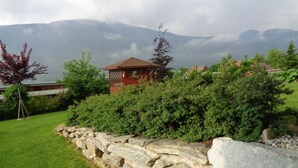 Un muro de piedra, un pabellón de madera y un área verde con montañas al fondo.