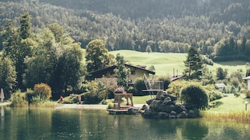 Blick auf einen See mit einem Haus, einem Steg und umgebender Vegetation.