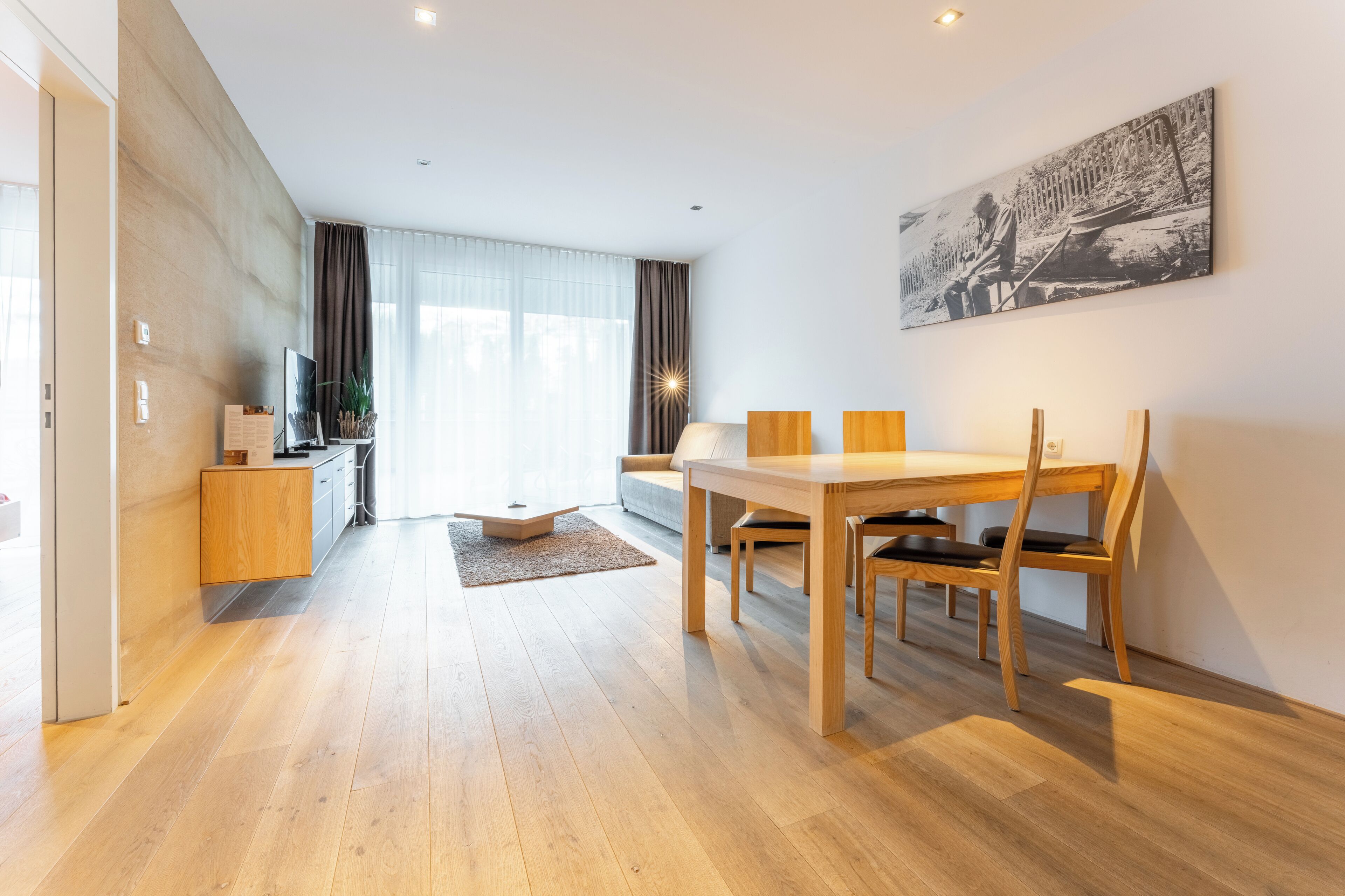 Una sala de estar moderna con una mesa de comedor de madera, sillas, un sofá y un televisor sobre un mueble de madera.