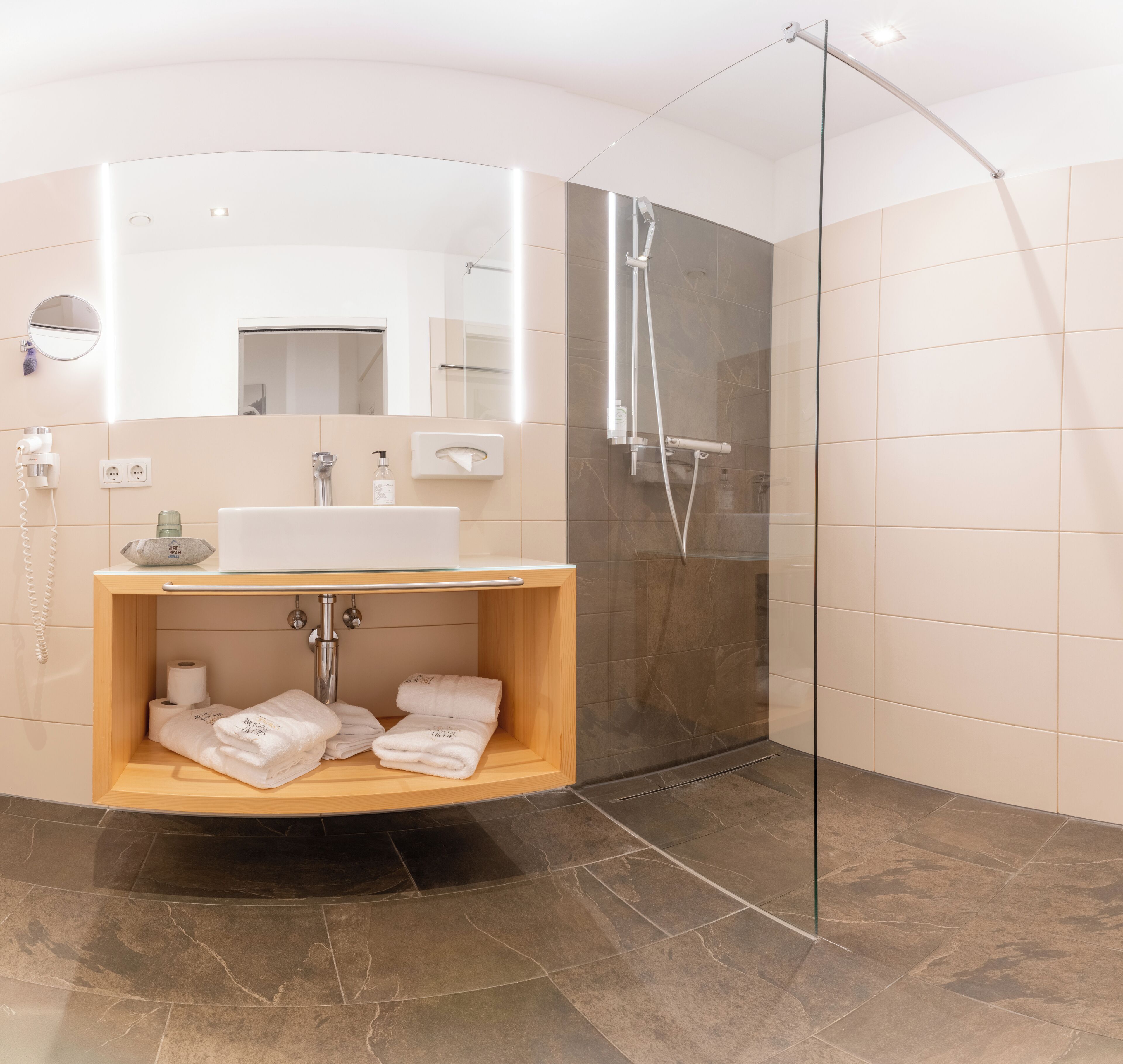A modern bathroom with a glass-enclosed shower, a wooden vanity with a sink, and a mirror.