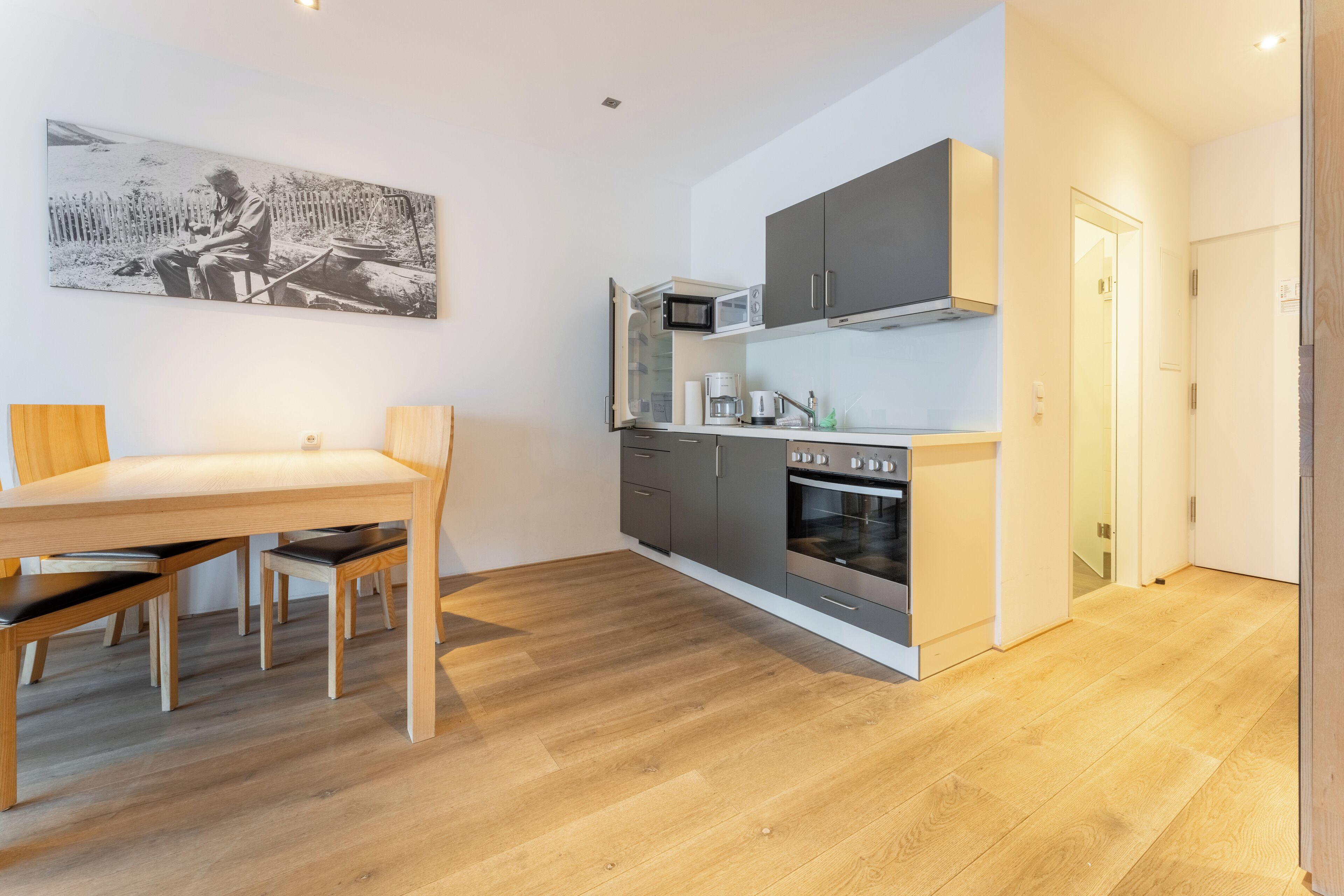 Une cuisine moderne avec des meubles gris, un four à micro-ondes et un four traditionnel. On y trouve une table à manger avec des chaises, et une photographie en noir et blanc accrochée au mur.