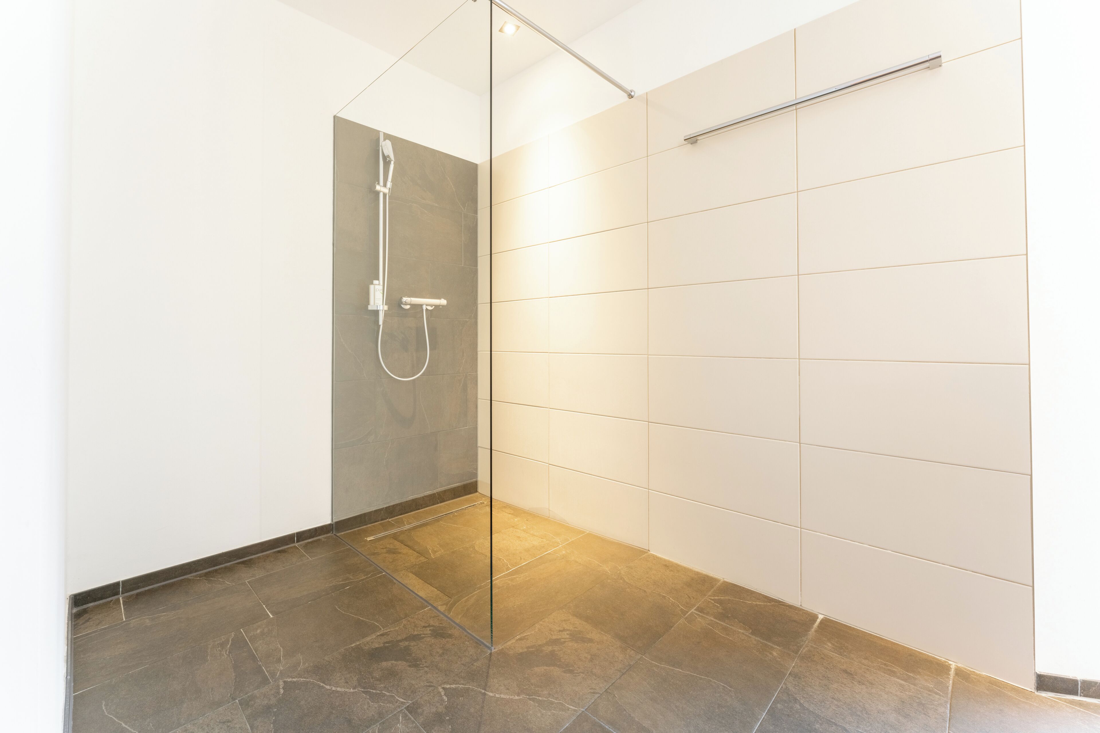 Ein zeitgemäßer Duschbereich mit Glasabtrennung, gefliesten Wänden und dunklem Boden.