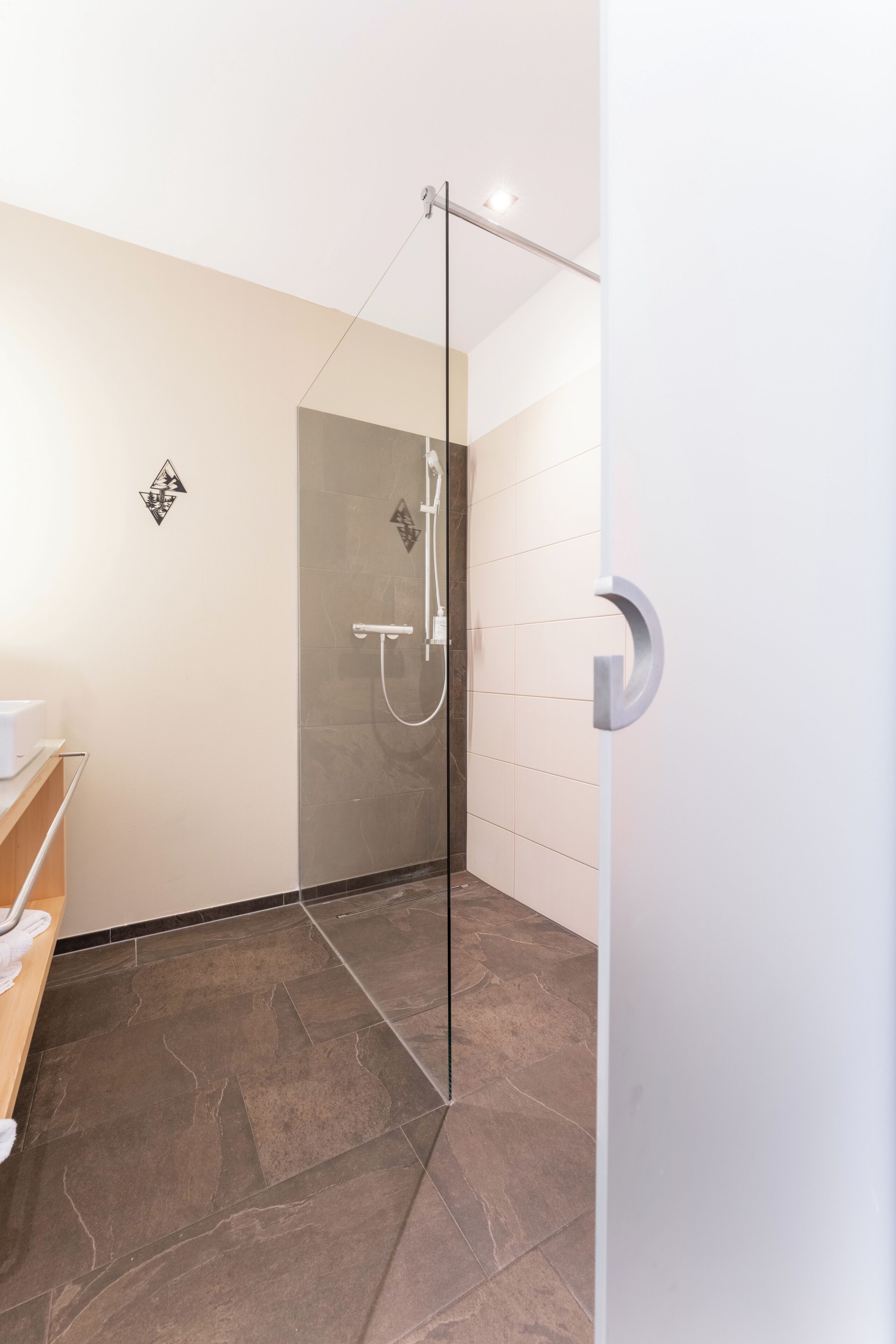 Un baño moderno con cabina de ducha de vidrio, piso de baldosas oscuras y pared blanca con diseño geométrico.