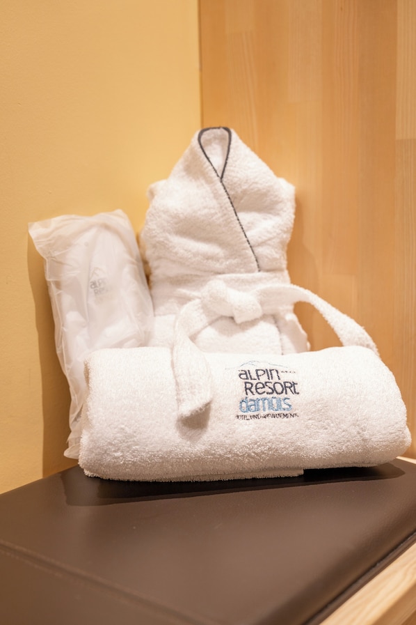 A white bathrobe and towel set with the text "Alpin Resort Damuli" on the towel.