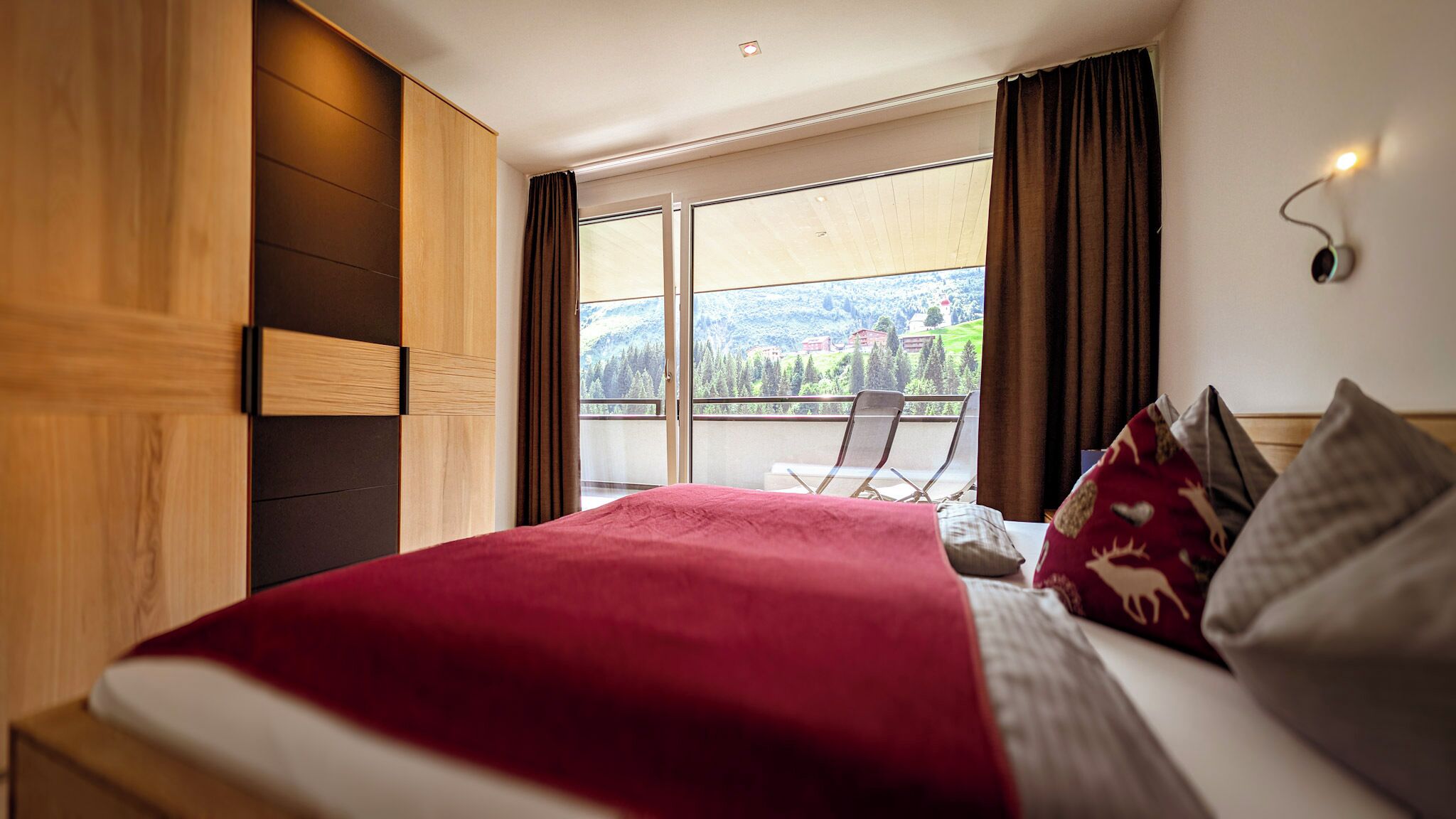 A bedroom with a large bed, a view of the outdoors, and a balcony with a chair.