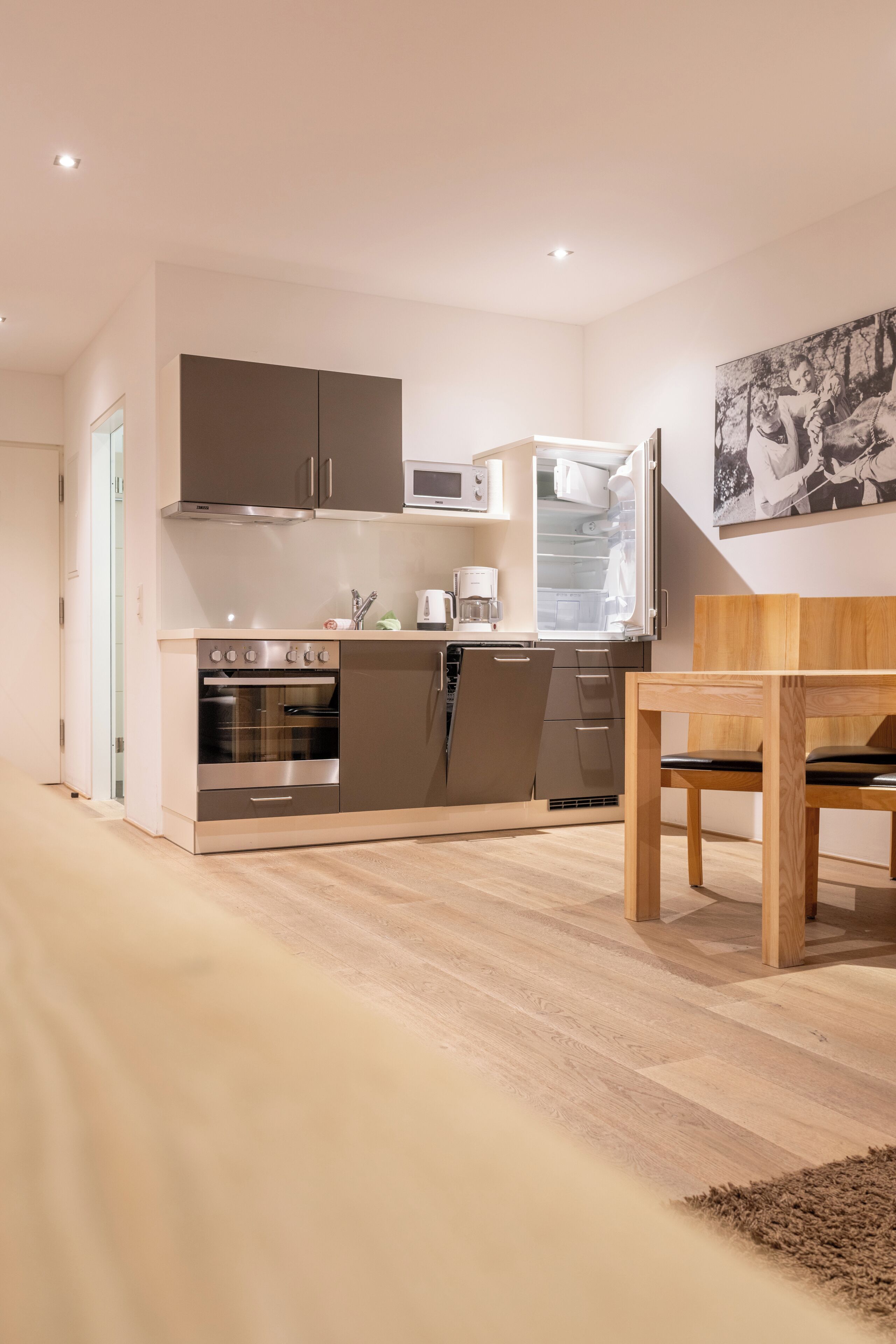 A modern kitchen with stainless steel appliances, a wooden dining table, and a large abstract painting on the wall.