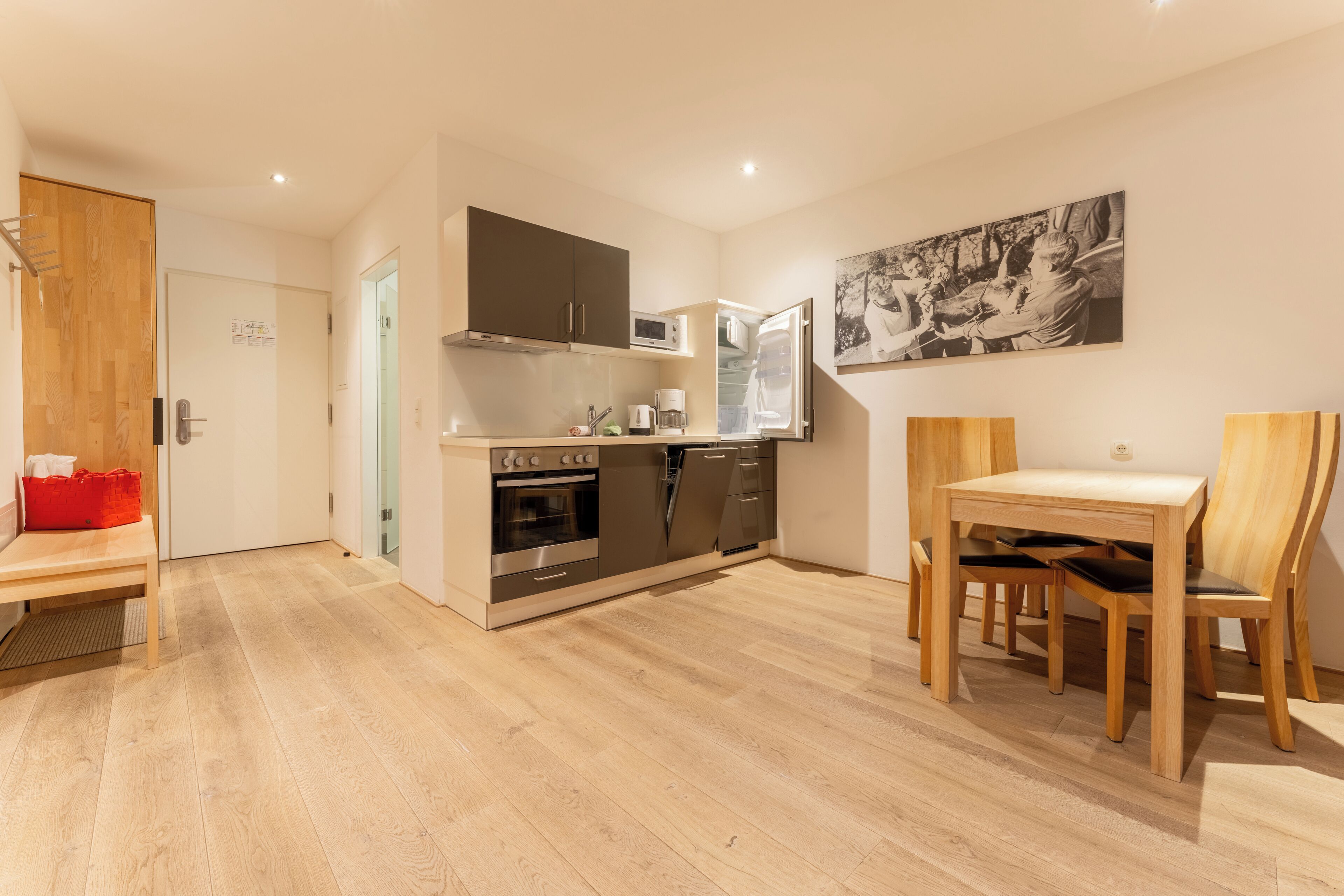 A modern kitchen with stainless steel appliances, a dining area with wooden furniture, and a wall-mounted artwork.