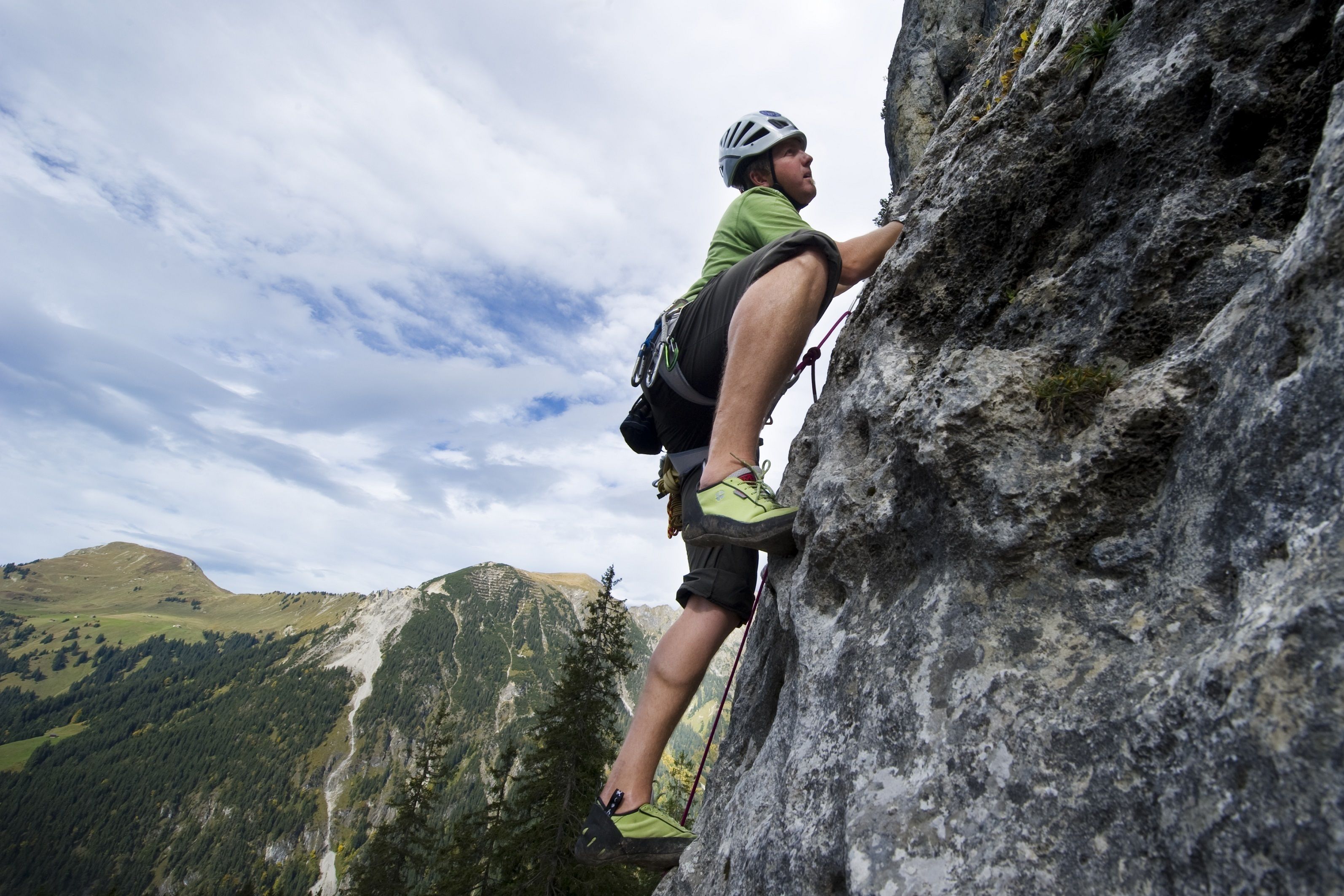 A person climbing a rock face with a mountainous landscape in the background.