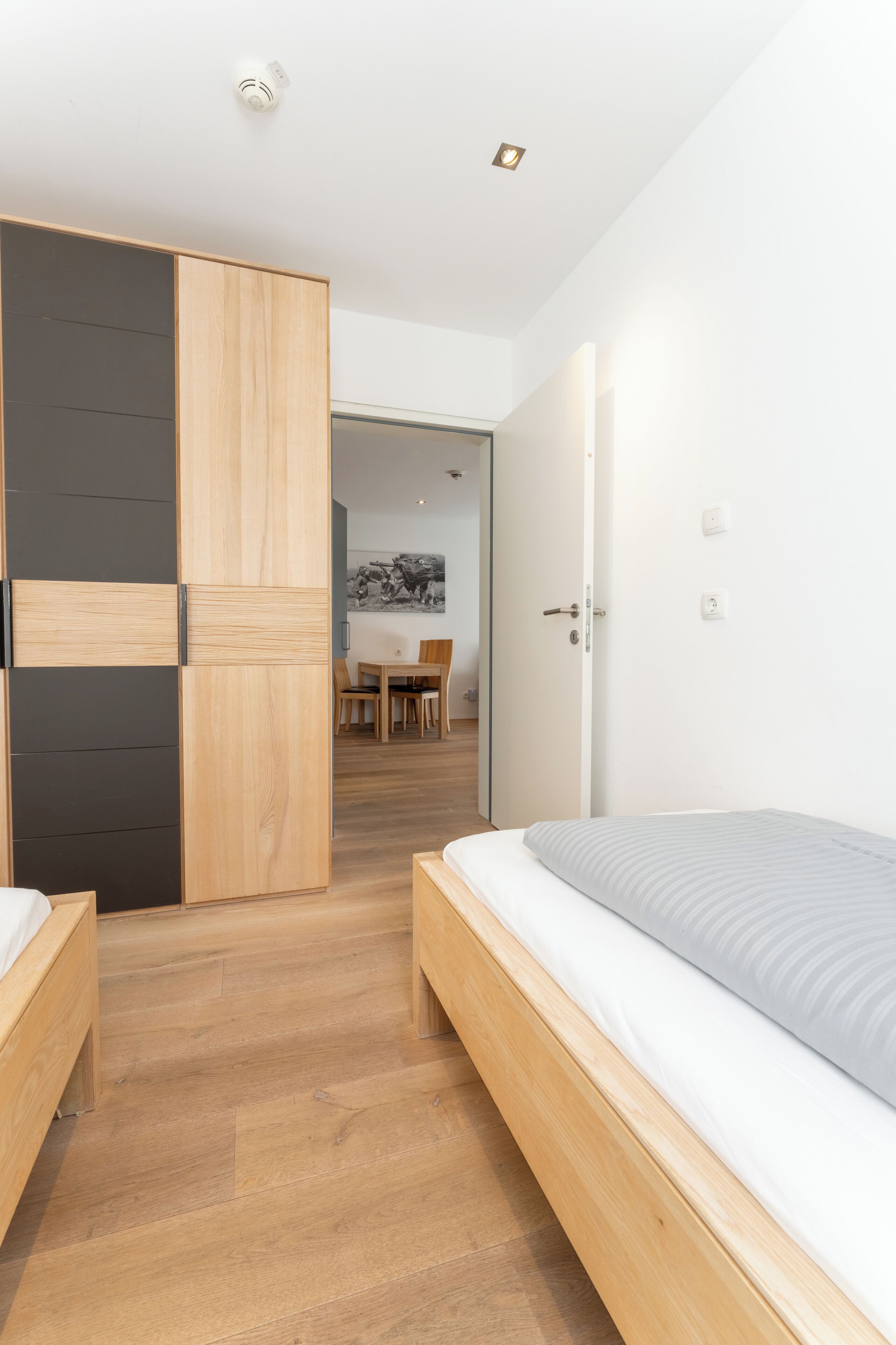 Een moderne slaapkamer met een houten bed, een inloopkast met schuifdeur en een eethoek op de achtergrond.