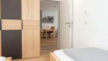 Een moderne slaapkamer met een houten bed, een inloopkast met schuifdeur en een eethoek op de achtergrond.