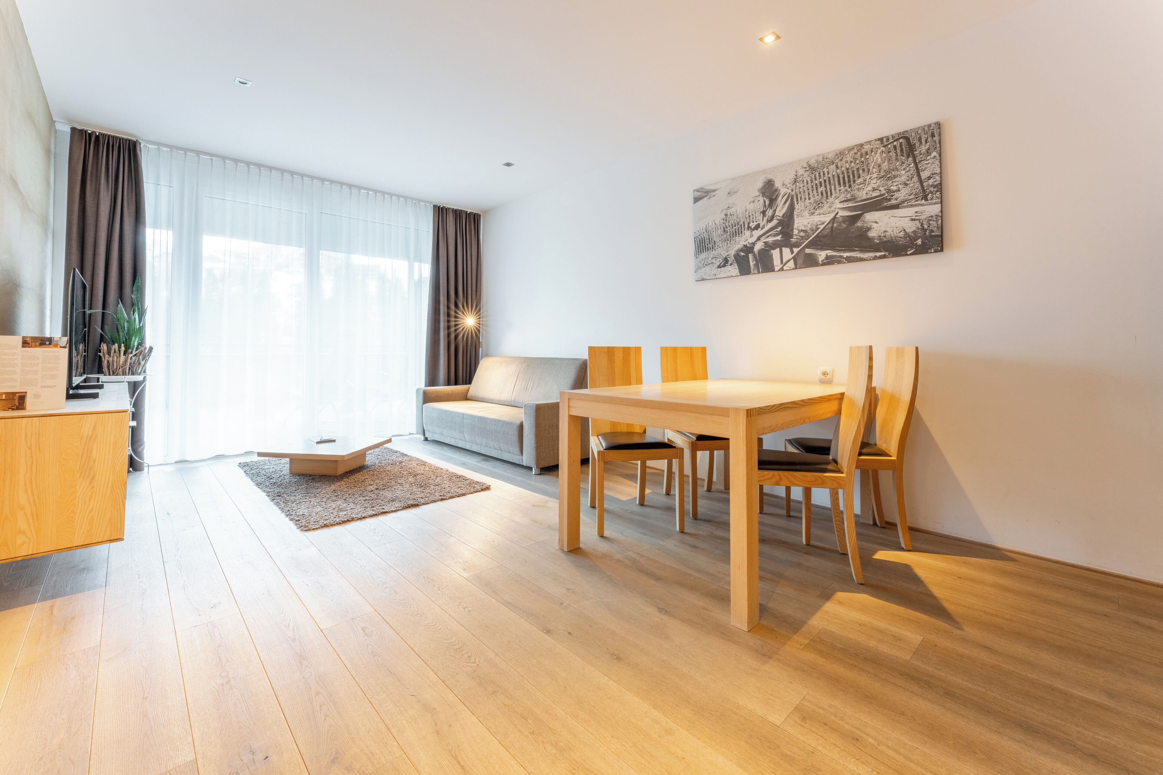 Ein modernes Wohnzimmer mit Holzesstisch, einer Couch und einem großen Fenster mit Vorhängen.