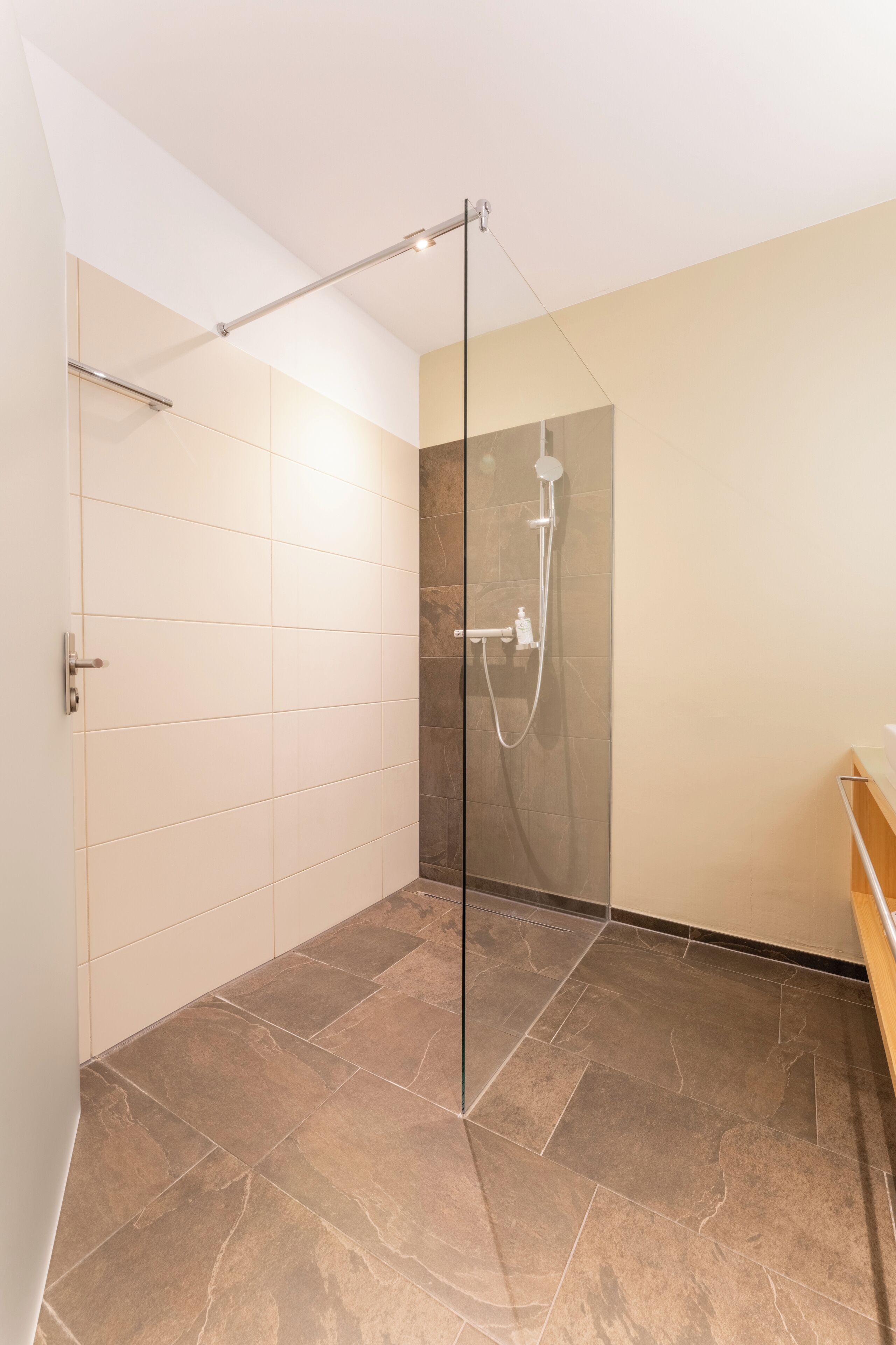 Une salle de bain moderne avec une douche à parois de verre, un sol carrelé et un banc en bois.