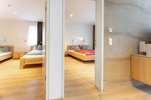 Una habitación de hotel moderna con suelo de madera, dos camas, un armario de madera y un escritorio.