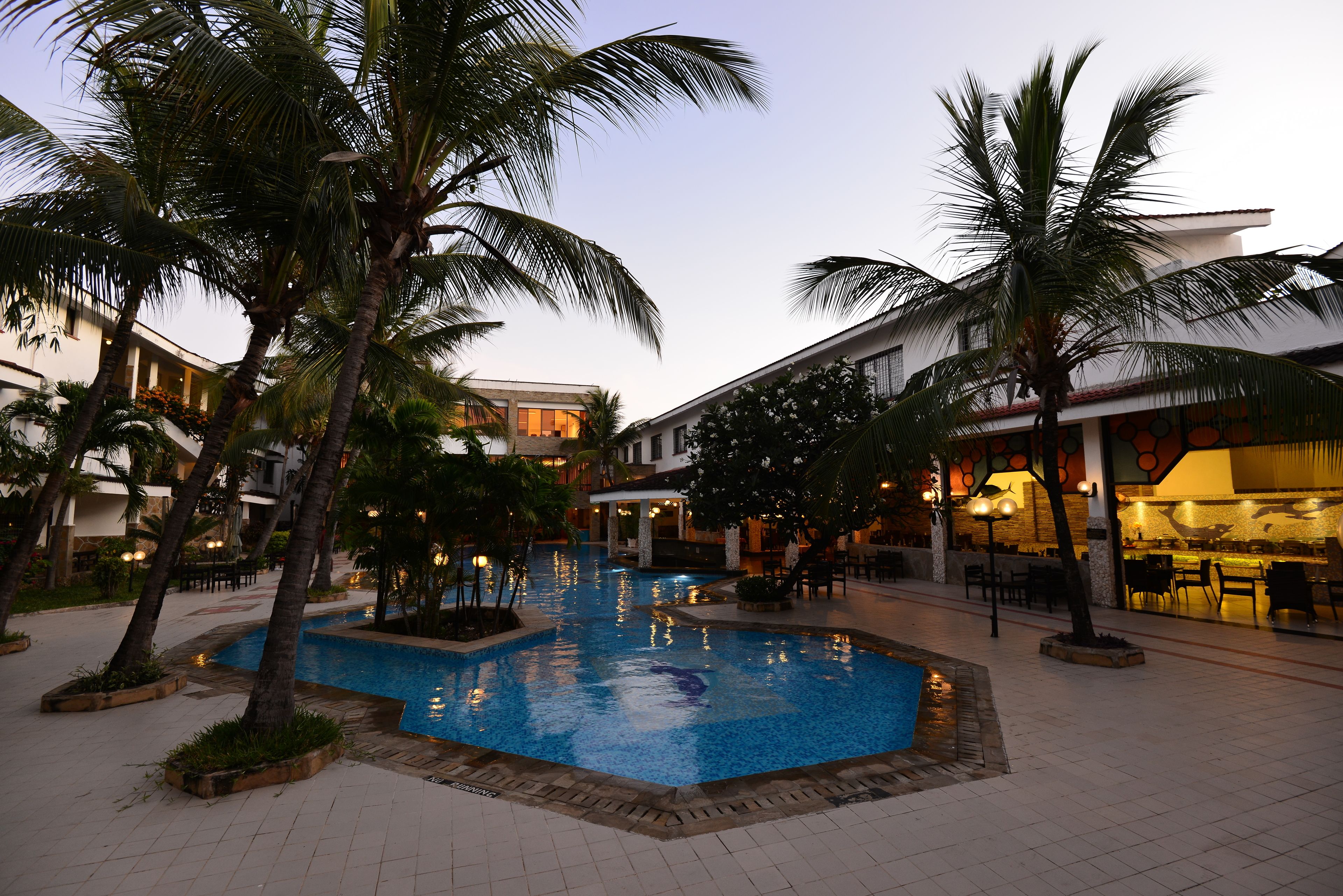 Une piscine entourée de palmiers et un restaurant avec une terrasse.