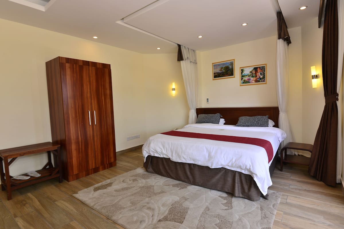 Un dormitorio con una cama grande, un armario de madera, un banco y dos lámparas fijadas a la pared.
