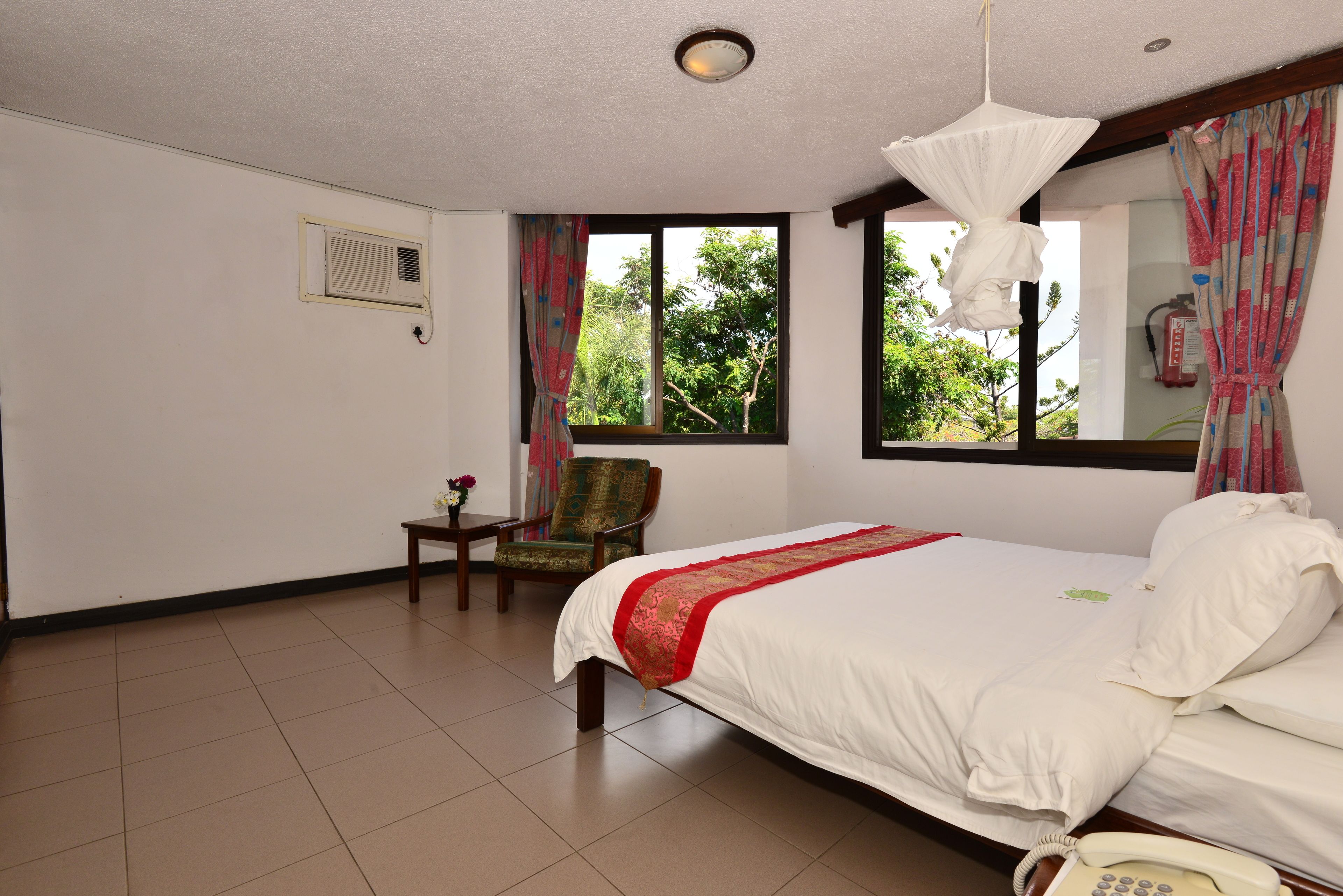 A hotel room with a large bed, a chair, a small table, and a window with curtains.
