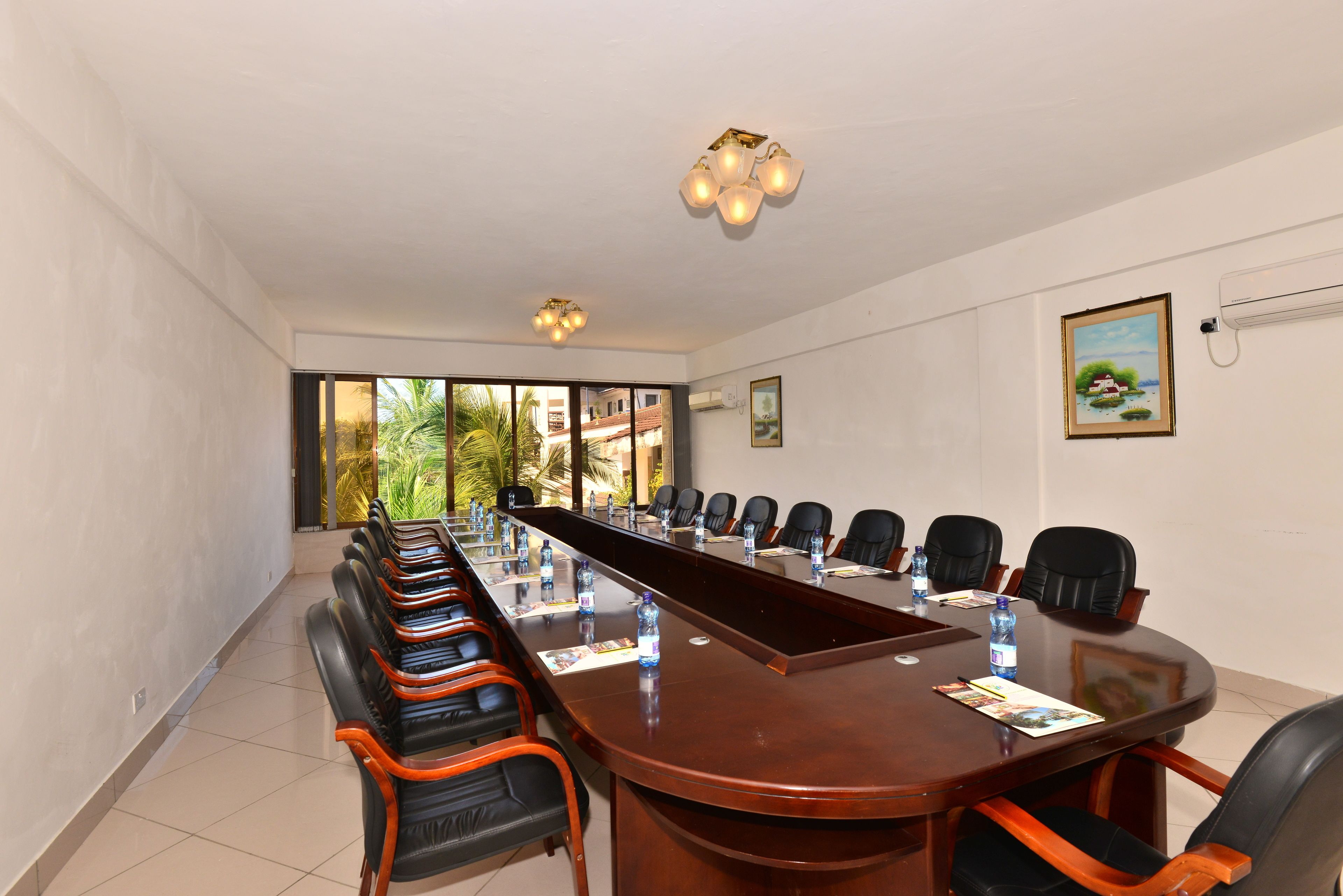 A conference room with a long table, chairs, and a view of palm trees outside.