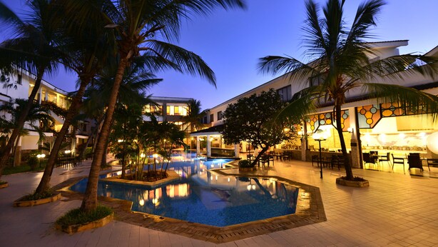 A pool area with palm trees, a bar, and outdoor seating. - Baobab Holiday Resort (Mombasa)