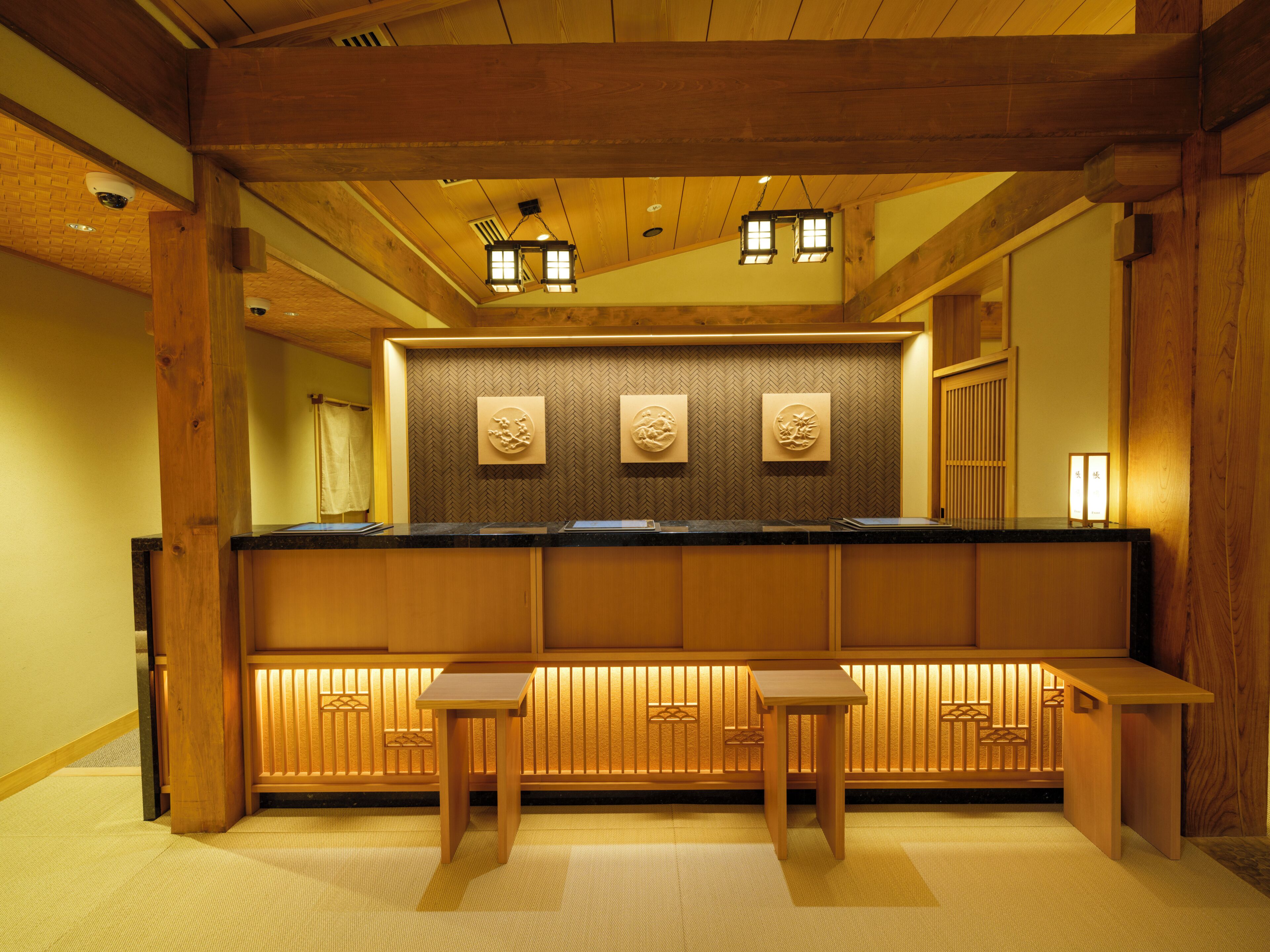 A traditional Japanese-style interior with wooden beams, tatami flooring, and a reception desk with stools.