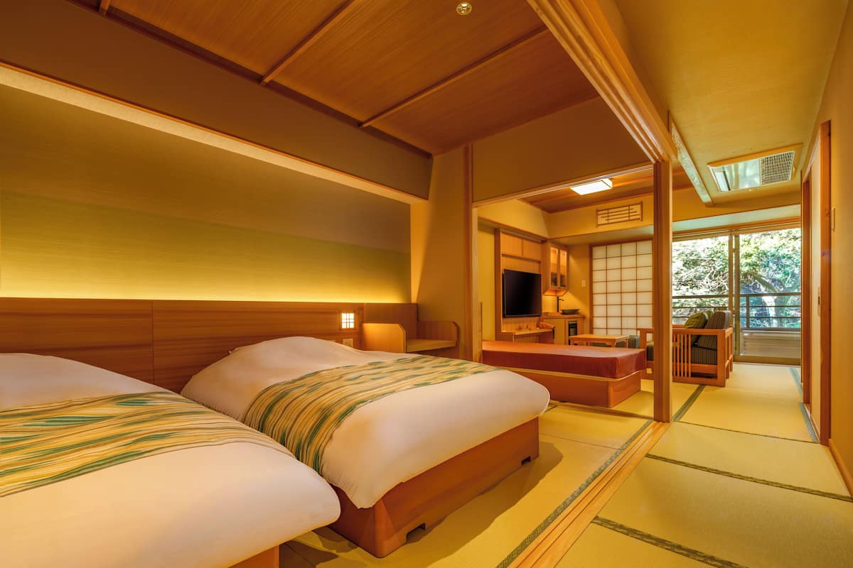 A traditional Japanese-style room with two beds, a television, and a sliding door leading to a balcony.