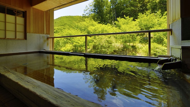 Un onsen japonais traditionnel, avec un intérieur en bois et une vue sur une végétation luxuriante.