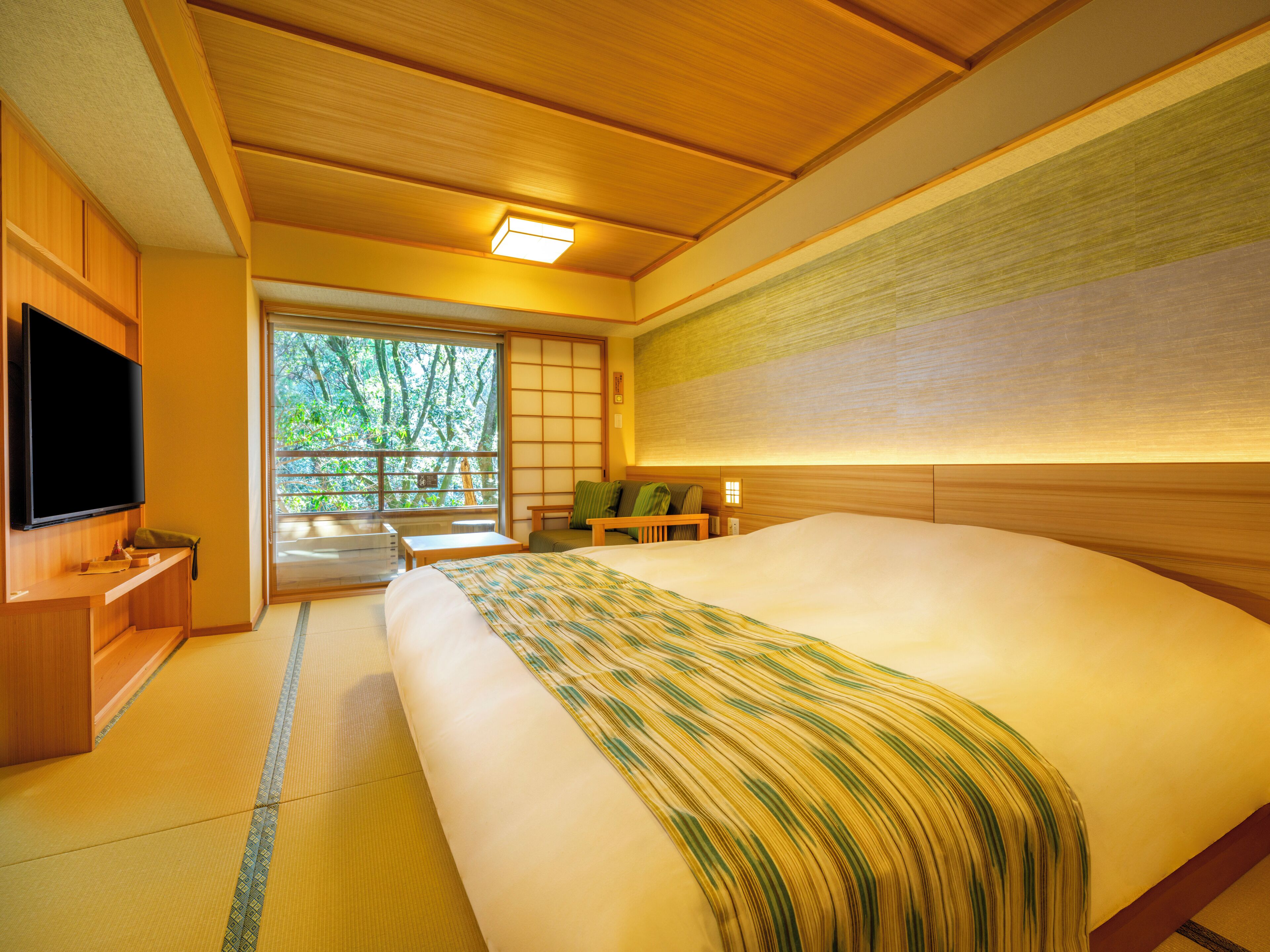 A traditional Japanese-style room with tatami flooring, a large bed with a striped blanket, a television, and a sliding door leading to a balcony.