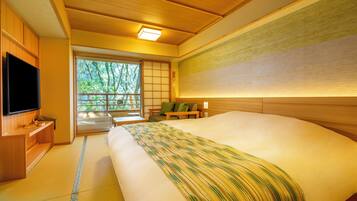 A traditional Japanese-style room with tatami flooring, a large bed with a striped blanket, a television, and a sliding door leading to a balcony.