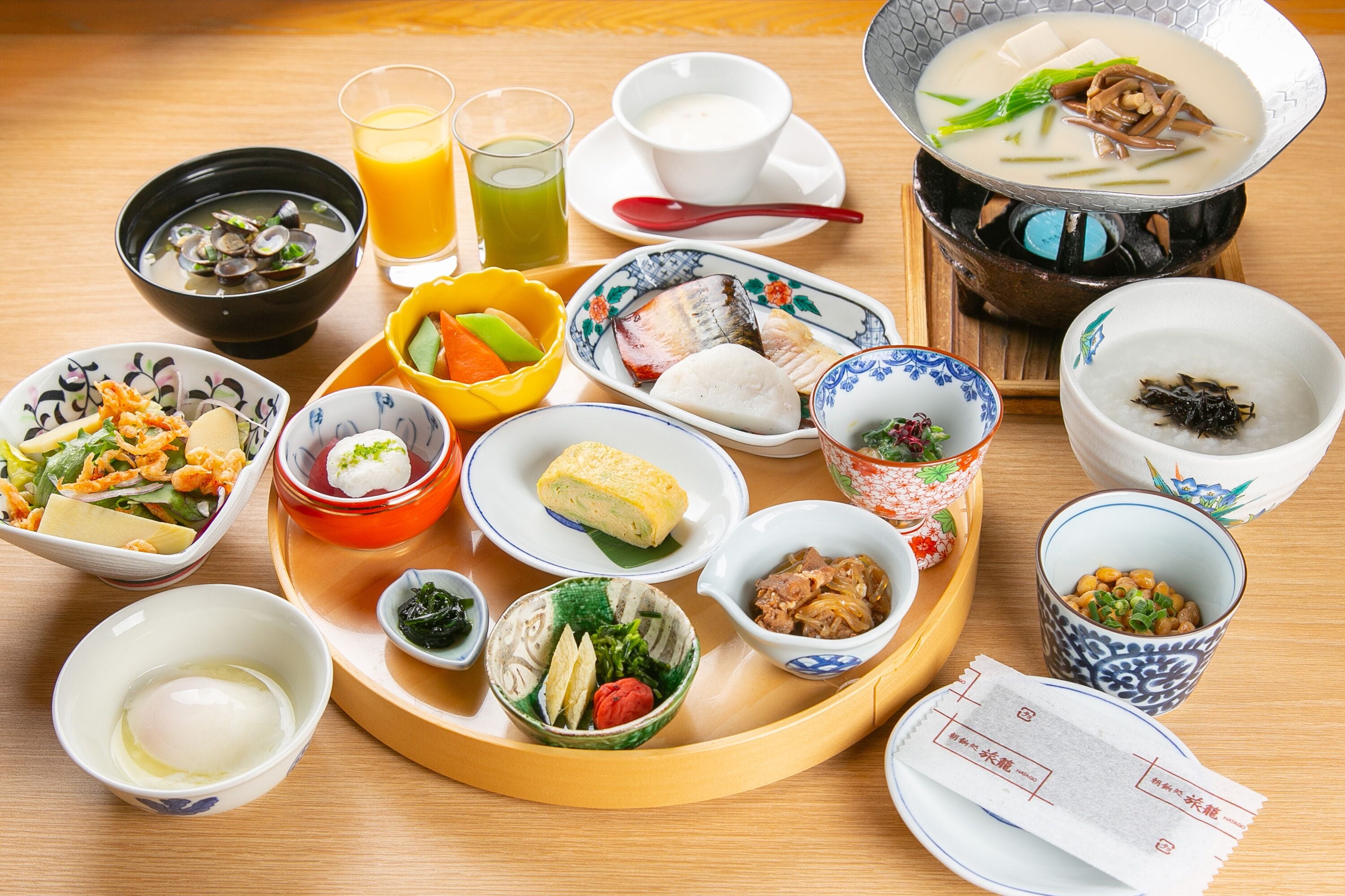 A variety of Japanese dishes on a wooden table, including a hot pot, bowls of soup, and plates of sashimi.